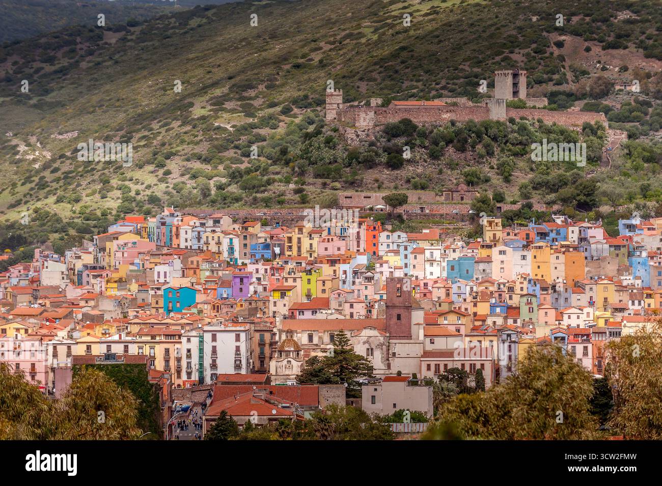 Vue panoramique sur la ville colorée de Bosa nichée dans les collines de Sardaigne, Italie, avec des ruines de château médiéval au-dessus et une végétation luxuriante autour Banque D'Images
