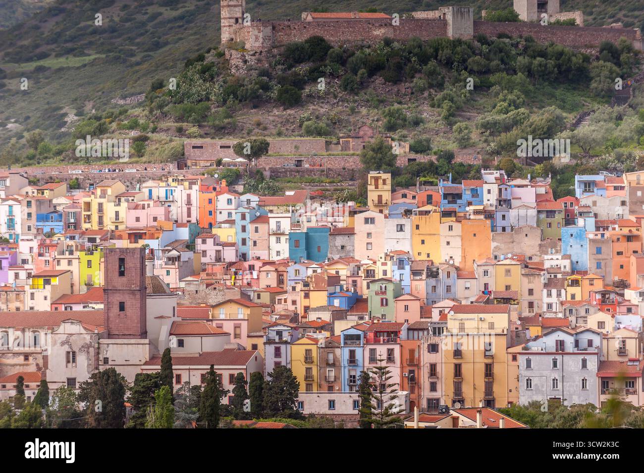 Vue panoramique sur la ville colorée de Bosa nichée dans les collines de Sardaigne, Italie, avec des ruines de château médiéval au-dessus et une végétation luxuriante autour. Banque D'Images