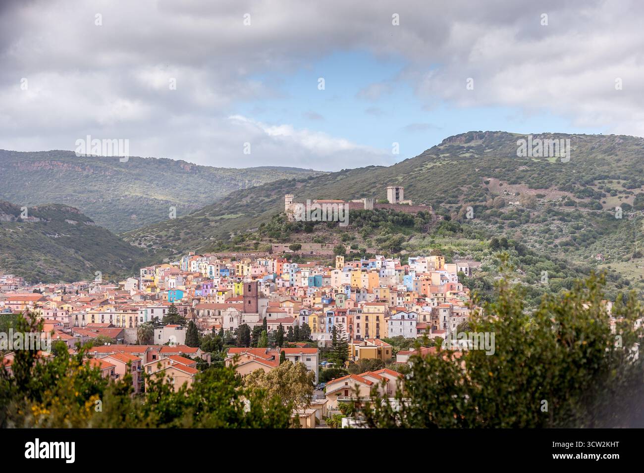 Vue panoramique sur la ville colorée de Bosa nichée dans les collines de Sardaigne, Italie, avec des ruines de château médiéval au-dessus et une végétation luxuriante autour. Banque D'Images