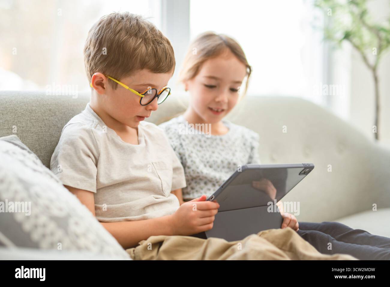 Un portrait d'un groupe d'enfants, les enfants sont assis sur un canapé à la maison, en utilisant une tablette Banque D'Images