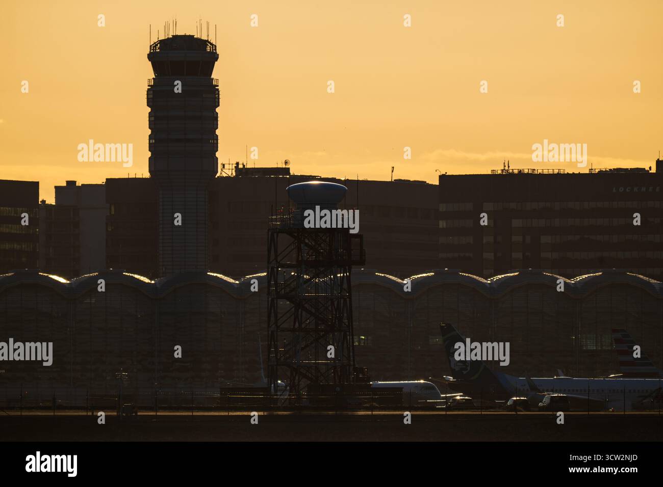 Tour de contrôle de l'aéroport national Reagan à Sunset Washington DC // WASHINGTON DC — la tour de contrôle du trafic aérien et le terminal de l'aéroport national Ronald Reagan Washington (DCA) sont dessinés contre le soleil couchant. Cet aéroport principal dessert la région métropolitaine de Washington. La scène est vue depuis Hains point, une zone de loisirs au confluent des rivières Potomac et Anacostia. Les queues des avions, y compris Alaska Airlines et American Airlines, sont visibles près du toit arqué distinctif du terminal. Un bâtiment Lockheed Martin fait également partie de la ligne d'horizon lointaine. Banque D'Images