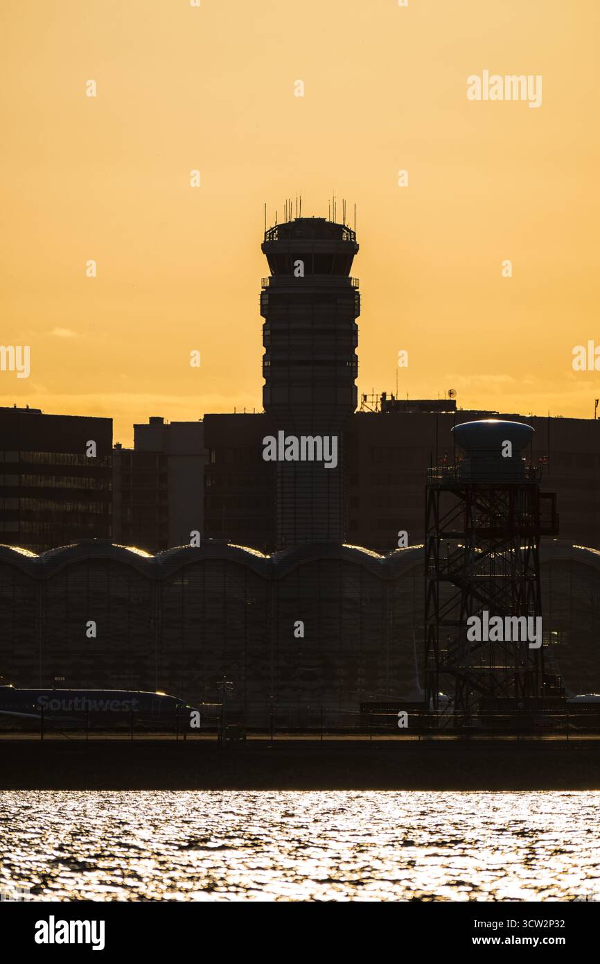 Tour de contrôle de l'aéroport national Reagan à Sunset Washington DC // WASHINGTON DC — la tour de contrôle du trafic aérien et les bâtiments du terminal de l'aéroport national Ronald Reagan Washington (DCA) sont dessinés contre le soleil couchant. Cet aéroport très fréquenté dessert la région métropolitaine de Washington D.C. et est situé à Arlington, en Virginie, de l'autre côté du fleuve Potomac. La photographie capture l'aéroport depuis Hains point, une péninsule de Washington, D.C. située au confluent des rivières Potomac et Anacostia. Un avion de Southwest Airlines est partiellement visible sur le tarmac, ajoutant à la scène de l'aéroport. Banque D'Images