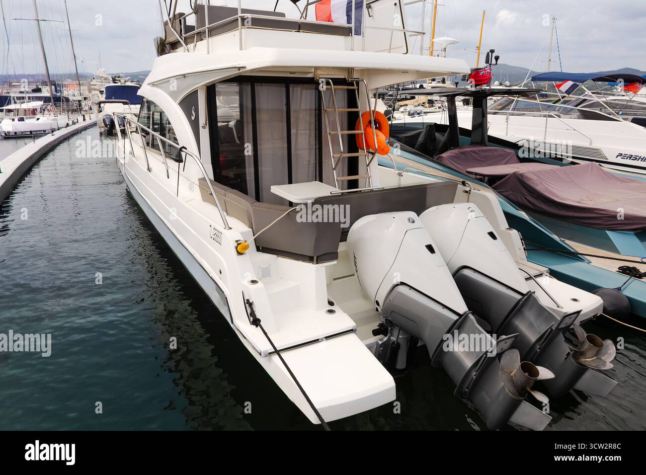 Un yacht flybridge moderne est amarré dans une marina, présentant deux moteurs hors-bord puissants sur la poupe. Banque D'Images