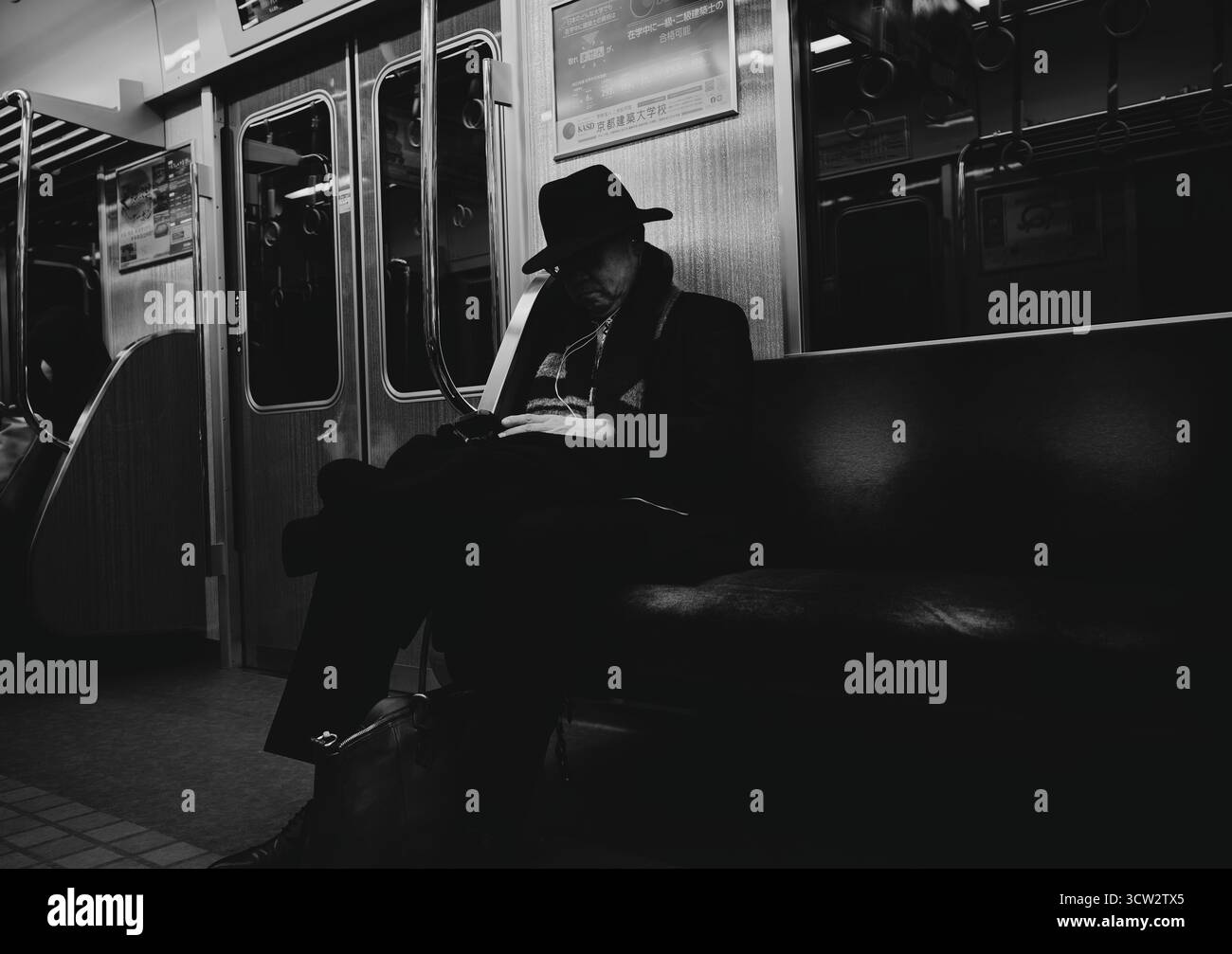 Un homme en costume sombre et chapeau repose tranquillement sur un train de métro d'Osaka en noir et blanc Banque D'Images