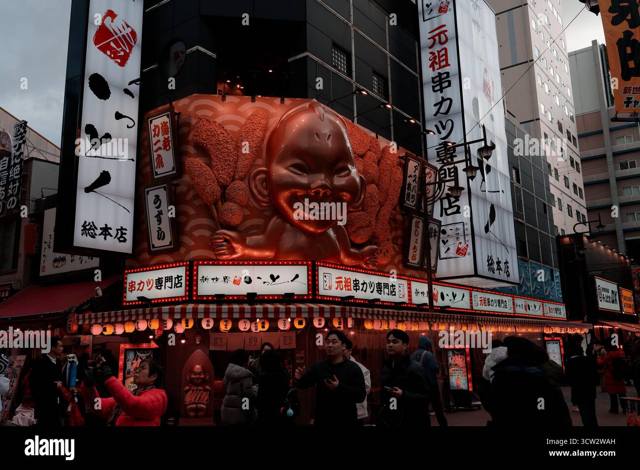 La devanture d’un restaurant kushikatsu dans le quartier Shinsekai d’Osaka, marquée par un visage géant et des lanternes lumineuses attirant les visiteurs curieux Banque D'Images