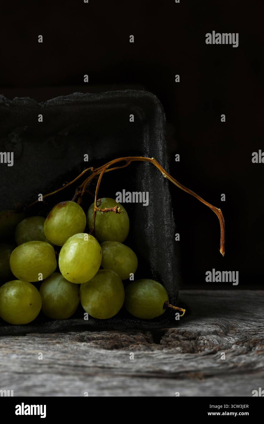 Un bouquet de raisins verts dans une boîte de produits en carton noir sur une table en bois rustique avec un fond de Balck. Banque D'Images