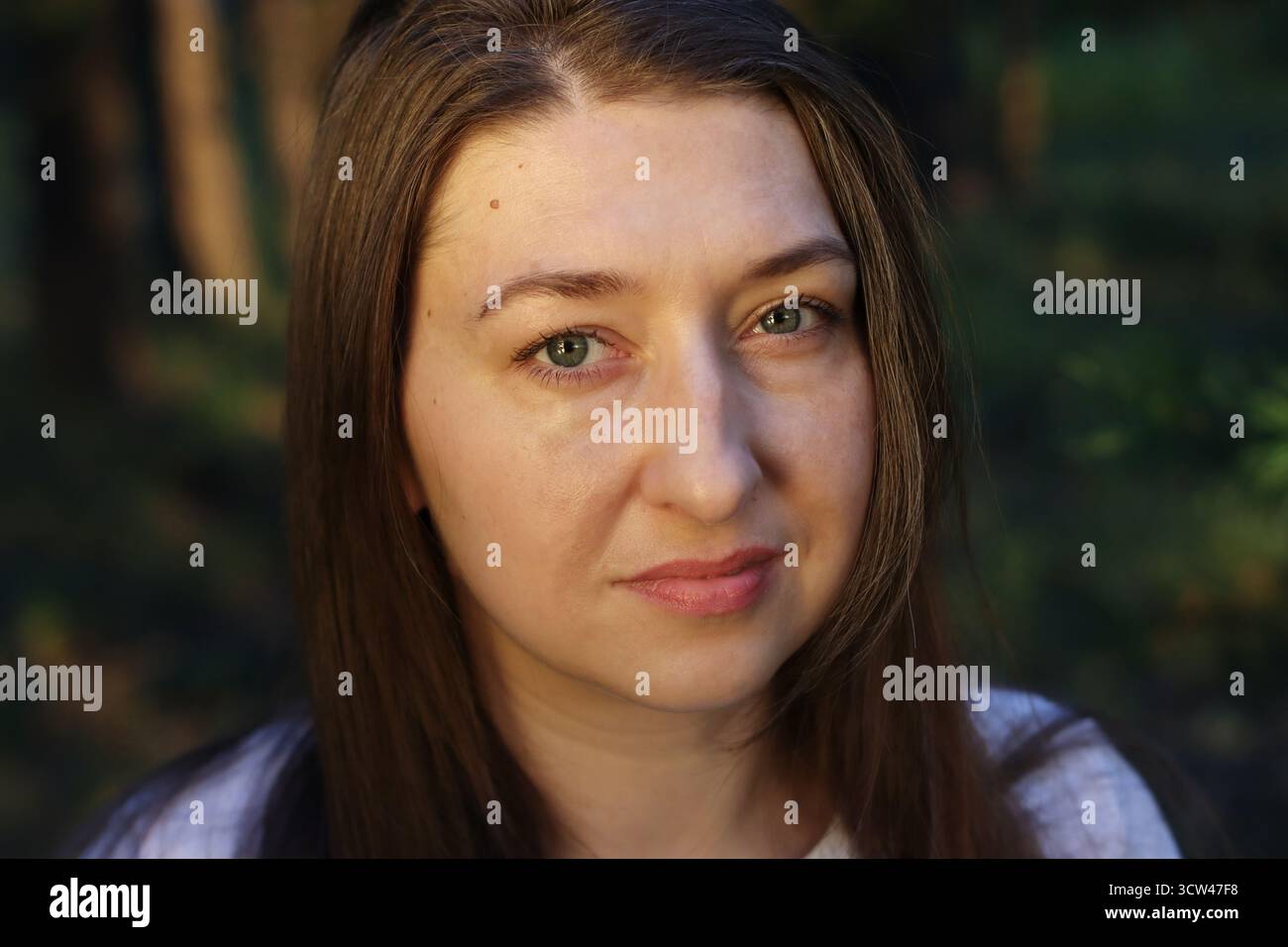 Gros plan portrait d'une jeune femme aux cheveux foncés avec des yeux clairs avec une expression naturelle et une lumière chaude. Nationalité slave. Émotion authentique et simpl Banque D'Images