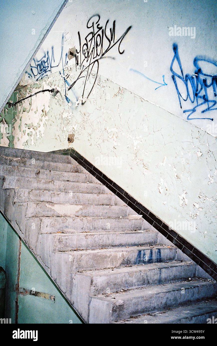 Escalier dans une usine abandonnée sans balustrade, marquée par plusieurs graffitis, capturés avec flash analogique pour un look industriel brut. Banque D'Images