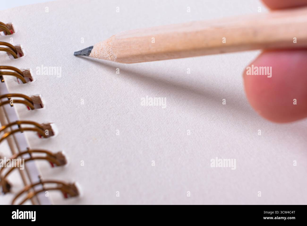 Gros plan des mains écrivant sur le bloc-notes en spirale. Main avec un crayon en bois se préparant à écrire sur un cahier vierge Banque D'Images