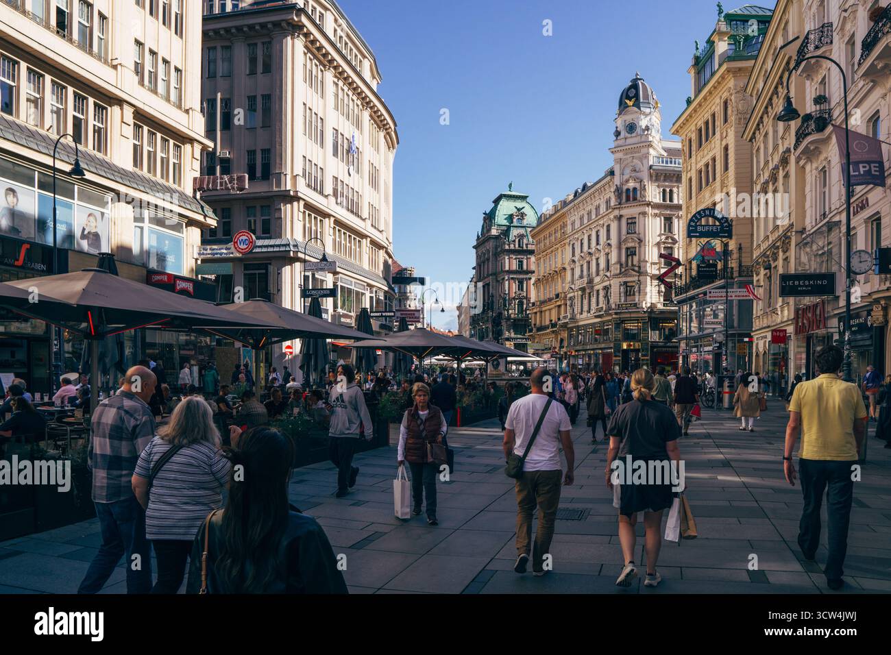 Les gens se promènent le long d'une rue animée de Vienne, entourée de beaux bâtiments historiques et de cafés en plein air animés pendant un après-midi ensoleillé. Banque D'Images