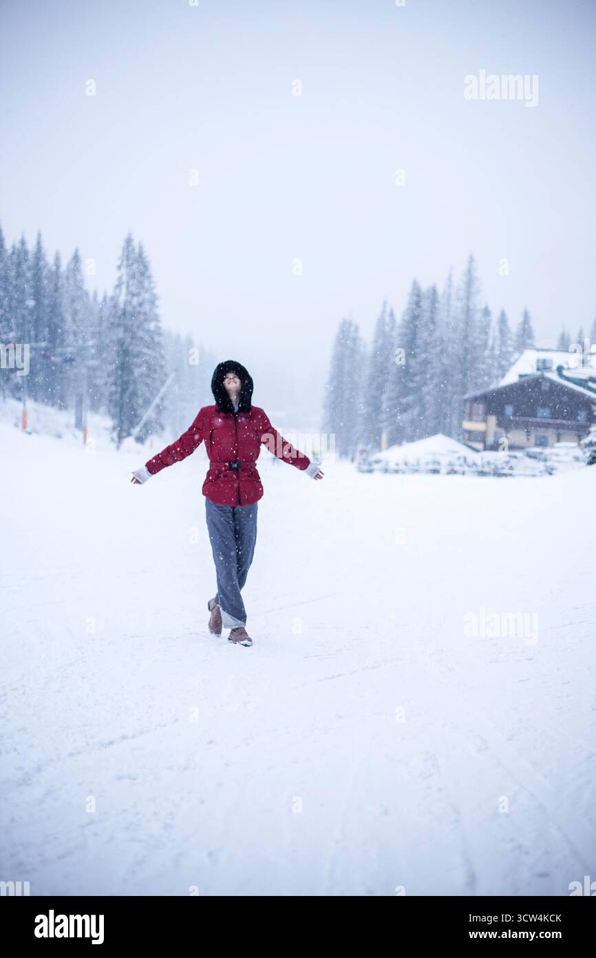 Portrait de belle femme en veste d'hiver rouge, tout en se tenant sur une piste de ski et en profitant de la neige et de la scène d'hiver. Modèle sportif, ski, snowboard. Banque D'Images