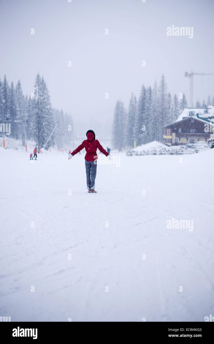 Portrait de femme méconnaissable en veste d'hiver rouge, tout en se tenant debout sur une piste de ski et en regardant les gens qui aiment les sports d'hiver. Modèle sportif en hiver Banque D'Images