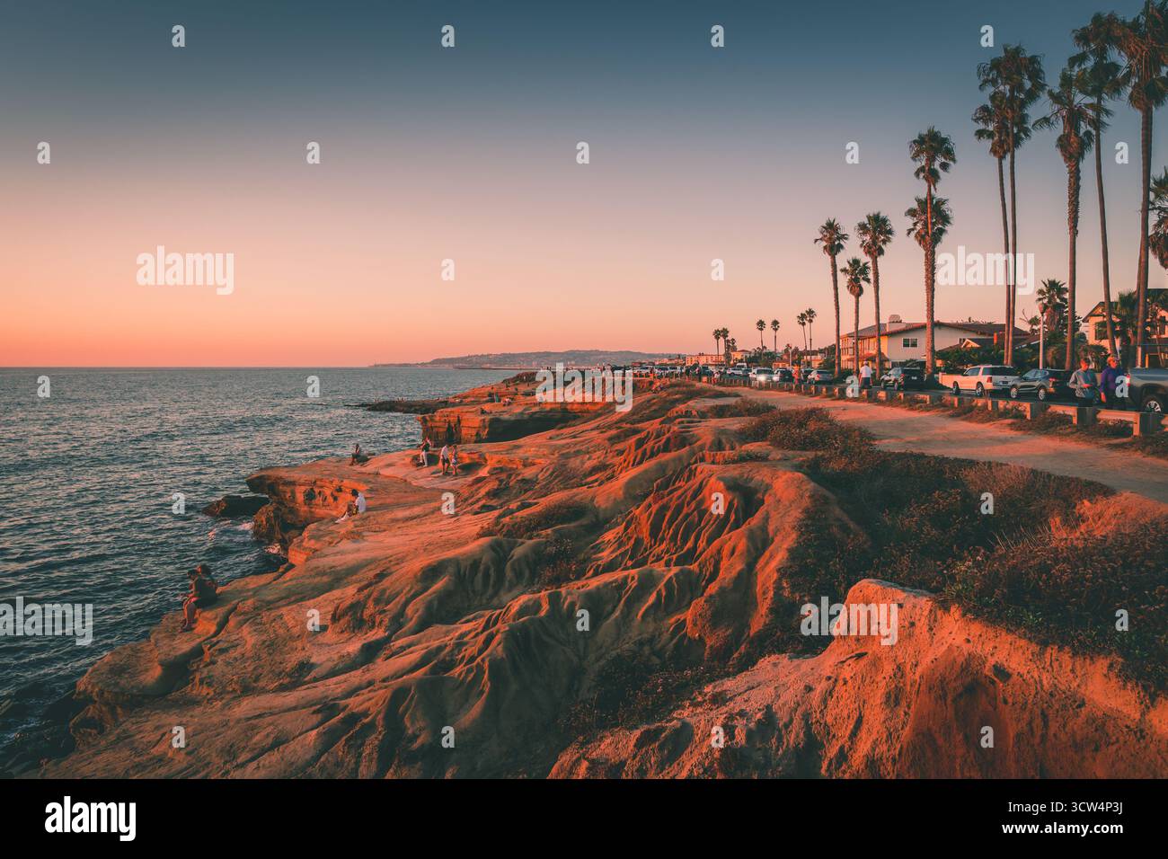 Les visiteurs profitent d'un magnifique coucher de soleil au bord de l'océan sur une falaise côtière, entourée de palmiers et de vues panoramiques, tandis que les couleurs remplissent le ciel. Banque D'Images