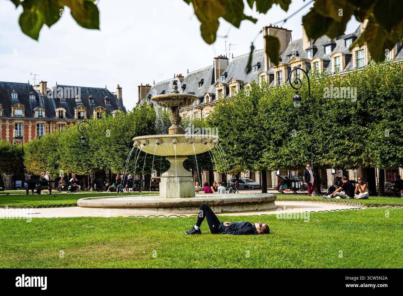 Les gens se détendent sur l'herbe à la place des Vosges dans le quartier du Marais pendant une journée d'été, l'une des plus anciennes et belles places de Paris, France Banque D'Images Les gens se détendent sur l'herbe à la place des Vosges dans le quartier du Marais pendant une journée d'été, l'une des plus anciennes et belles places de Paris, France Banque D'Images