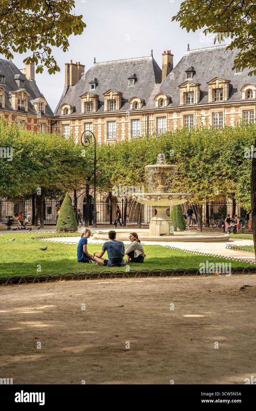 Les gens se détendent sur l'herbe à la place des Vosges dans le quartier du Marais pendant une journée d'été, l'une des plus anciennes et belles places de Paris, France Banque D'Images Les gens se détendent sur l'herbe à la place des Vosges dans le quartier du Marais pendant une journée d'été, l'une des plus anciennes et belles places de Paris, France Banque D'Images
