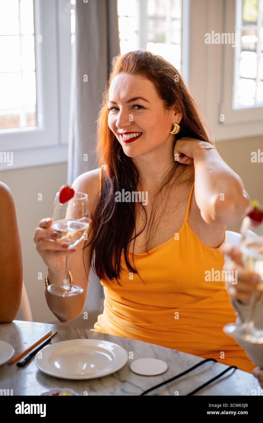 Femme en robe jaune souriant et tenant un verre à vin à l'intérieur Banque D'Images