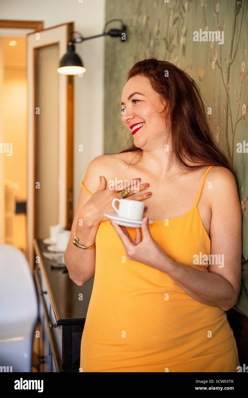 Femme en robe jaune buvant du café à la maison Banque D'Images