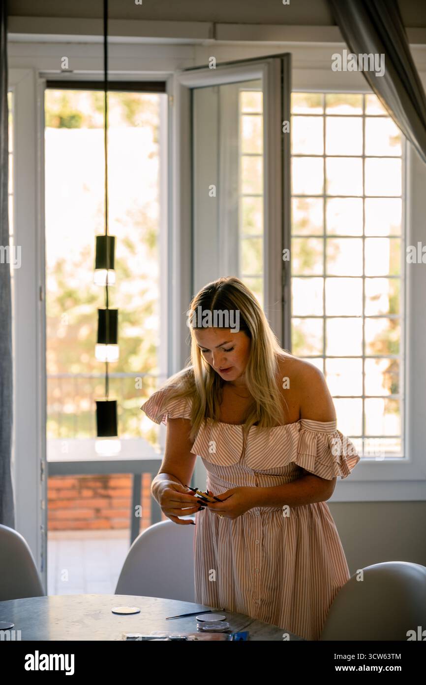 Femme en robe rayée debout près de la fenêtre à la maison Banque D'Images