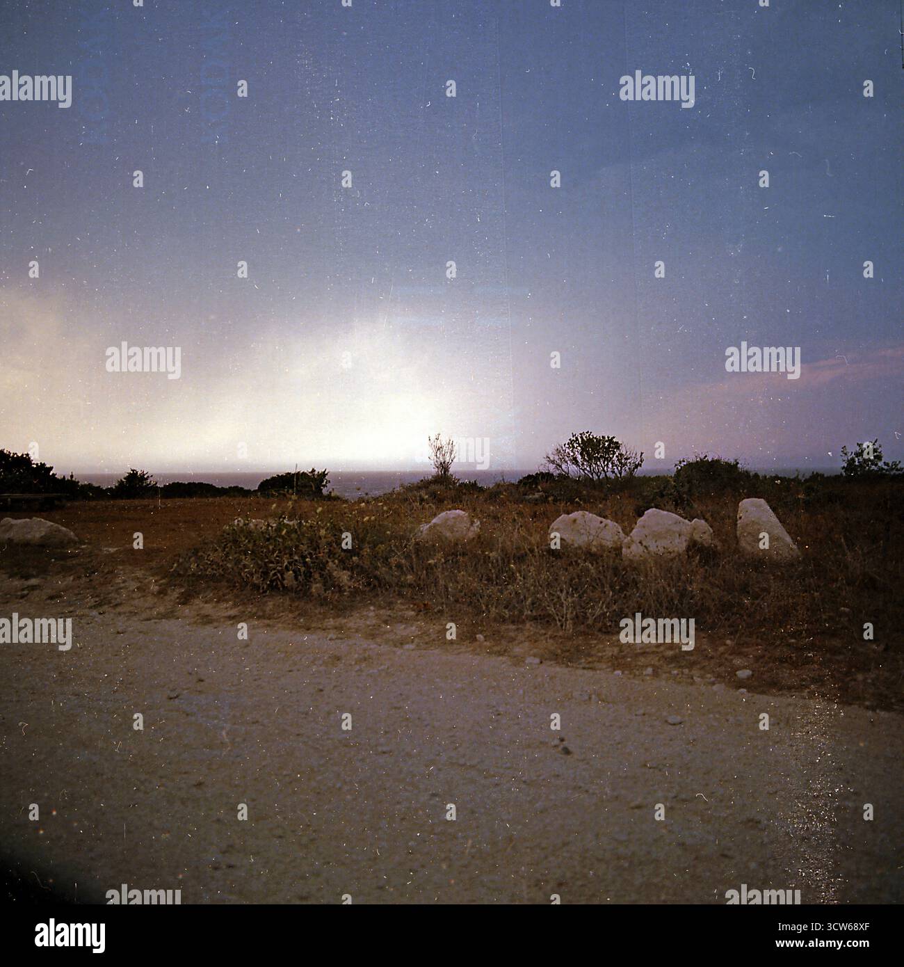 Paysage marin crépusculaire avec des rochers et une route au premier plan, capturé sur film moyen format et mal scanné avec des artefacts analogiques et numériques visibles Banque D'Images