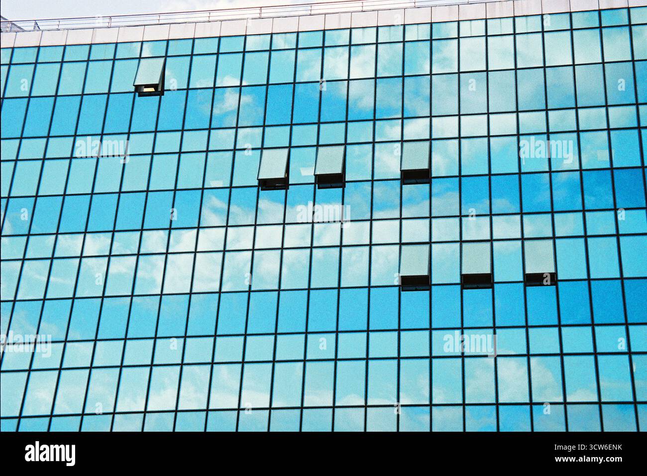 Immeuble de bureaux entièrement vitré reflétant le ciel clair. Certaines fenêtres s'ouvrent, brisant la symétrie. L'architecture rencontre la nature dans un pur reflet. Banque D'Images