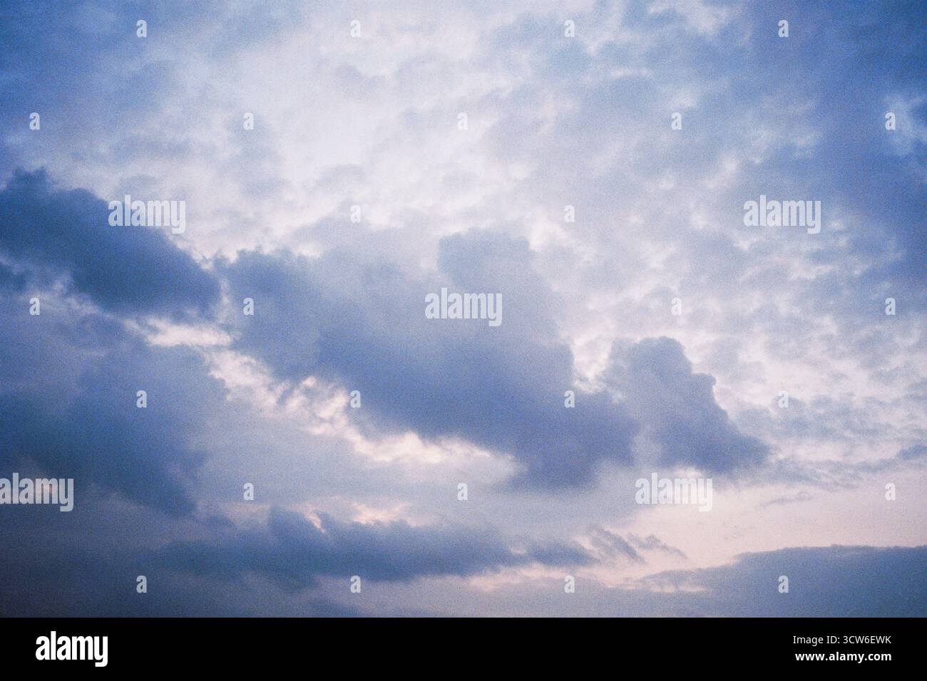 Des nuages foncés flottent contre un ciel lumineux et vide. Le contraste subtil et la douceur créent une tension visuelle tranquille. Tourné sur film analogique. Banque D'Images