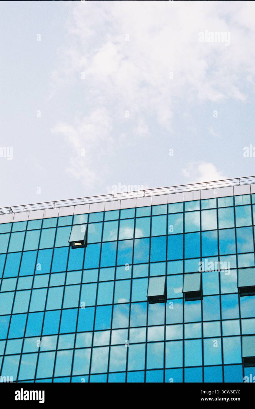 Plan vertical : bâtiment en demi-verre avec fenêtres ouvertes, demi-ciel lumineux avec nuages. Contraste ensoleillé entre structure et nature. Film. Banque D'Images