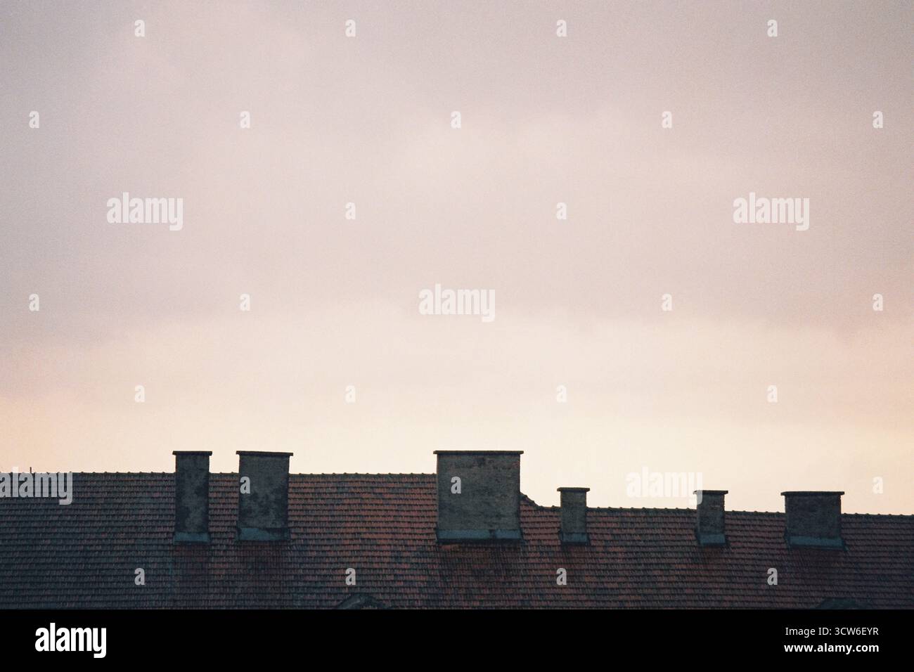 Toit sépia avec tuiles rouges et six cheminées sous un ciel lumineux et nuageux. Le soleil perce. Imitation et contraste sur film. Banque D'Images