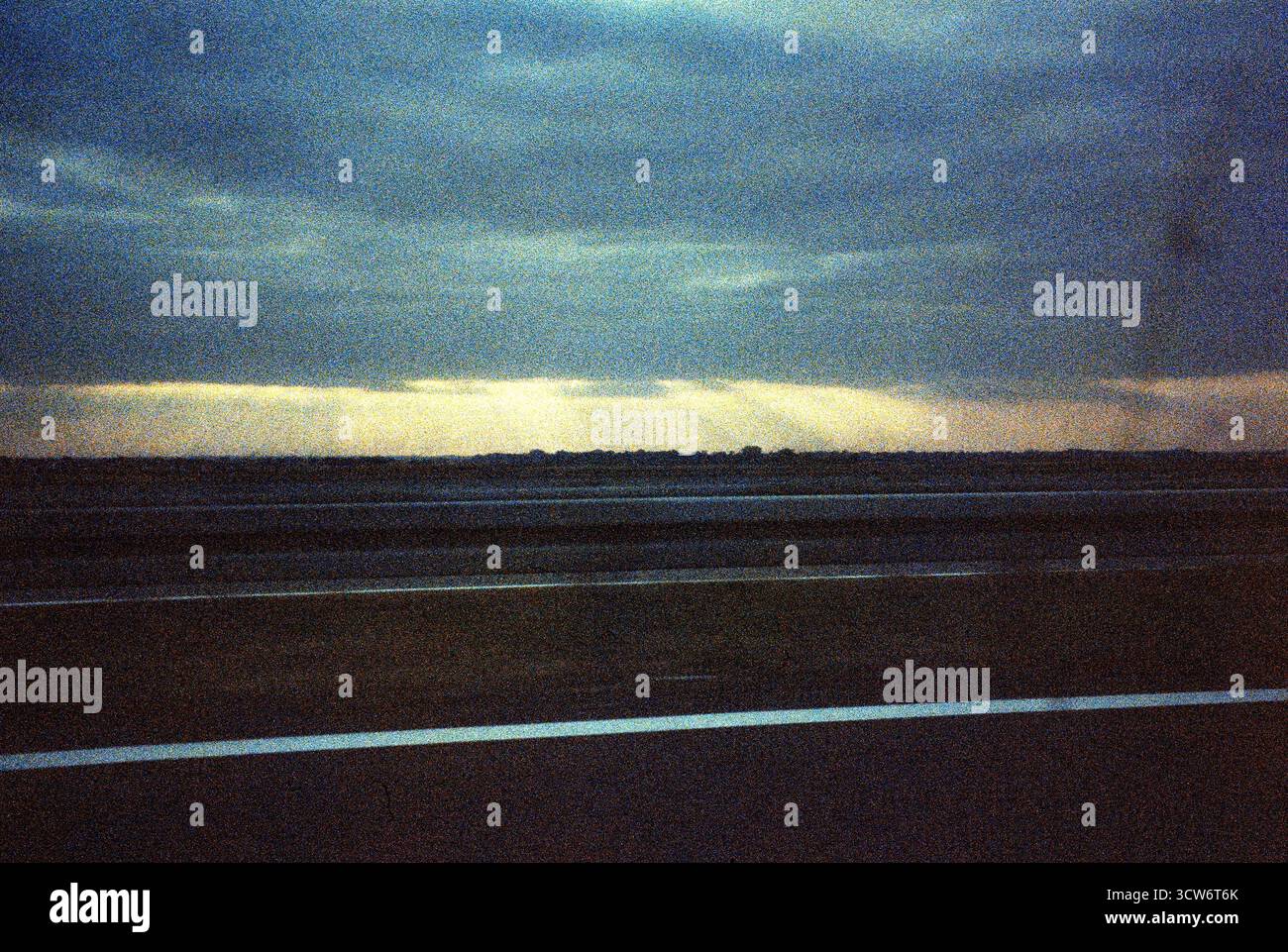 Coucher de soleil granuleux à travers la fenêtre passager d'une voiture en mouvement. Des nuages sombres se dessinent alors que les rayons du soleil brisent l'horizon. Tension tranquille au crépuscule. Banque D'Images