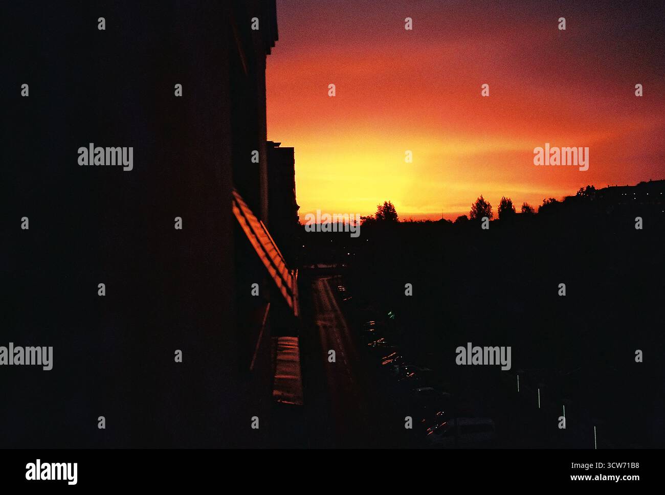 Scène d'aube à contraste élevé. Le ciel rouge profond domine le cadre, tandis que la terre en dessous reste dans l'obscurité. Ambiance audacieuse, dramatique, de style analogique. Banque D'Images