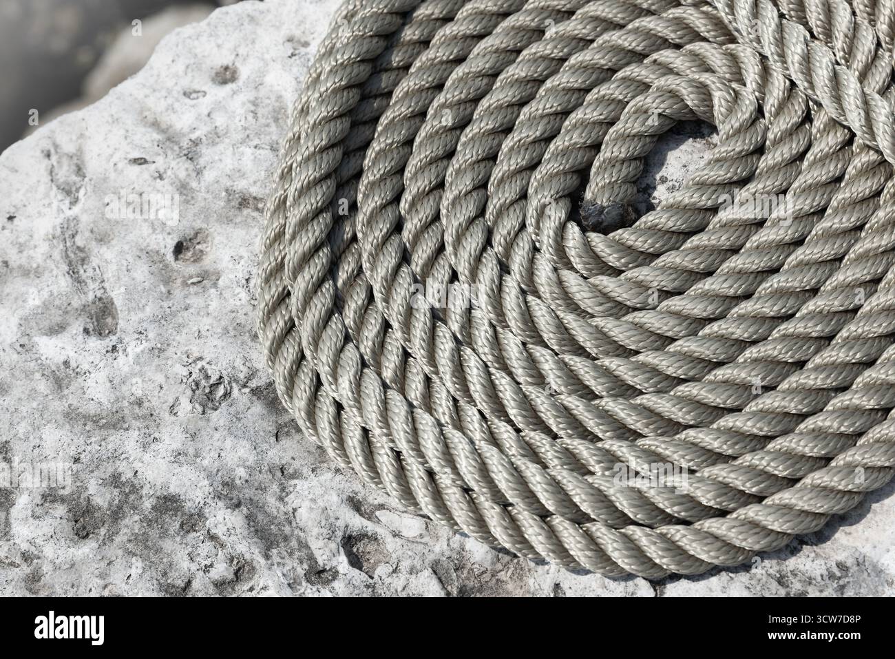 Une corde épaisse et grise soigneusement enroulée sur une surface rocheuse altérée. Ce gros plan capture la texture, la durabilité et l'attrait extérieur robuste adapté au nauti Banque D'Images