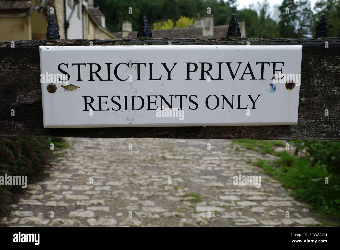 Panneau indiquant 'résidents strictement privés seulement' monté sur une porte en bois. L'arrière-plan présente un chemin pavé menant vers des bâtiments en pierre an Banque D'Images