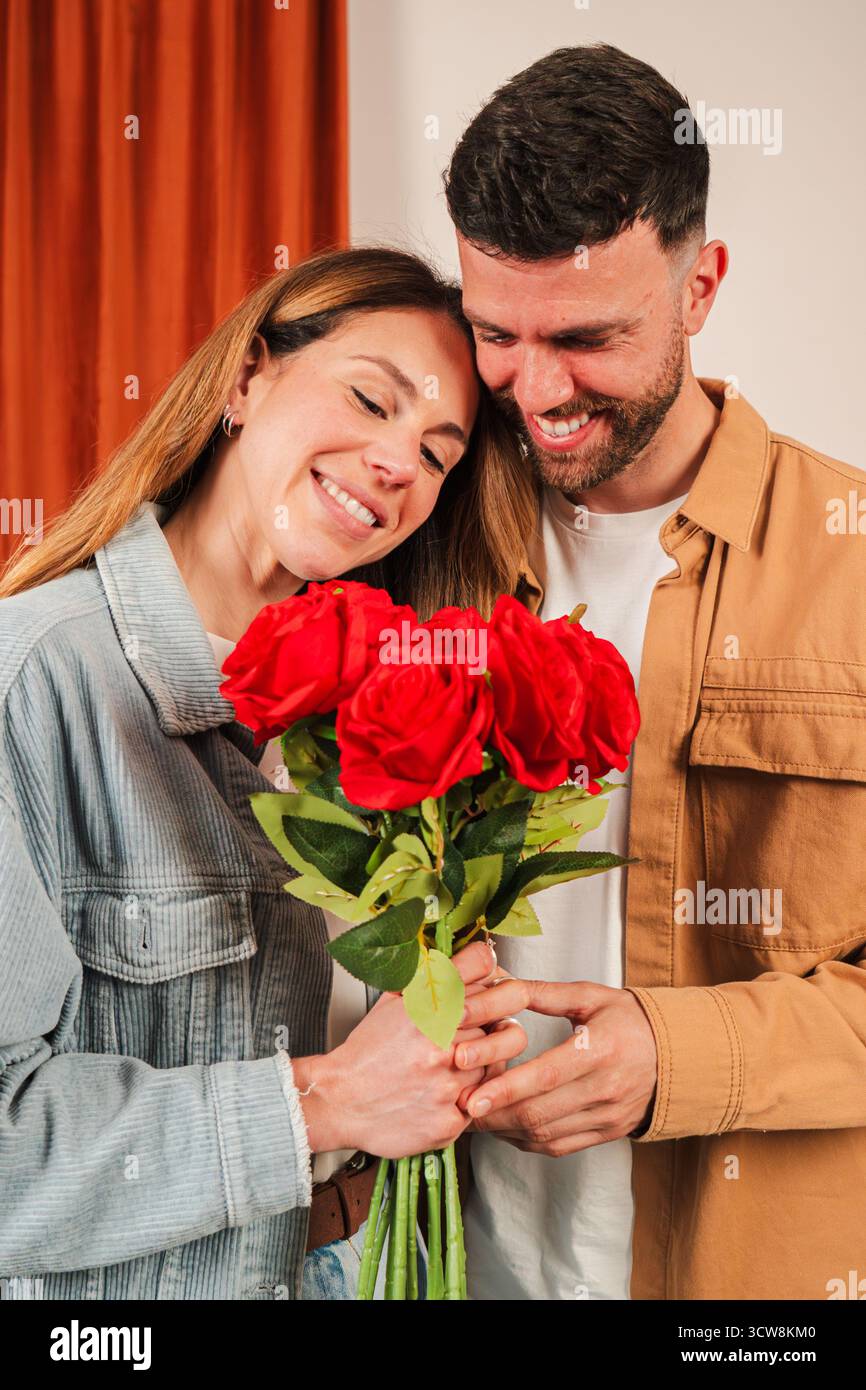 Un couple joyeux jouit d'un moment tendre alors qu'ils s'embrassent, tenant un bouquet étonnant de roses rouges rempli d'amour et d'affection, créant un Banque D'Images