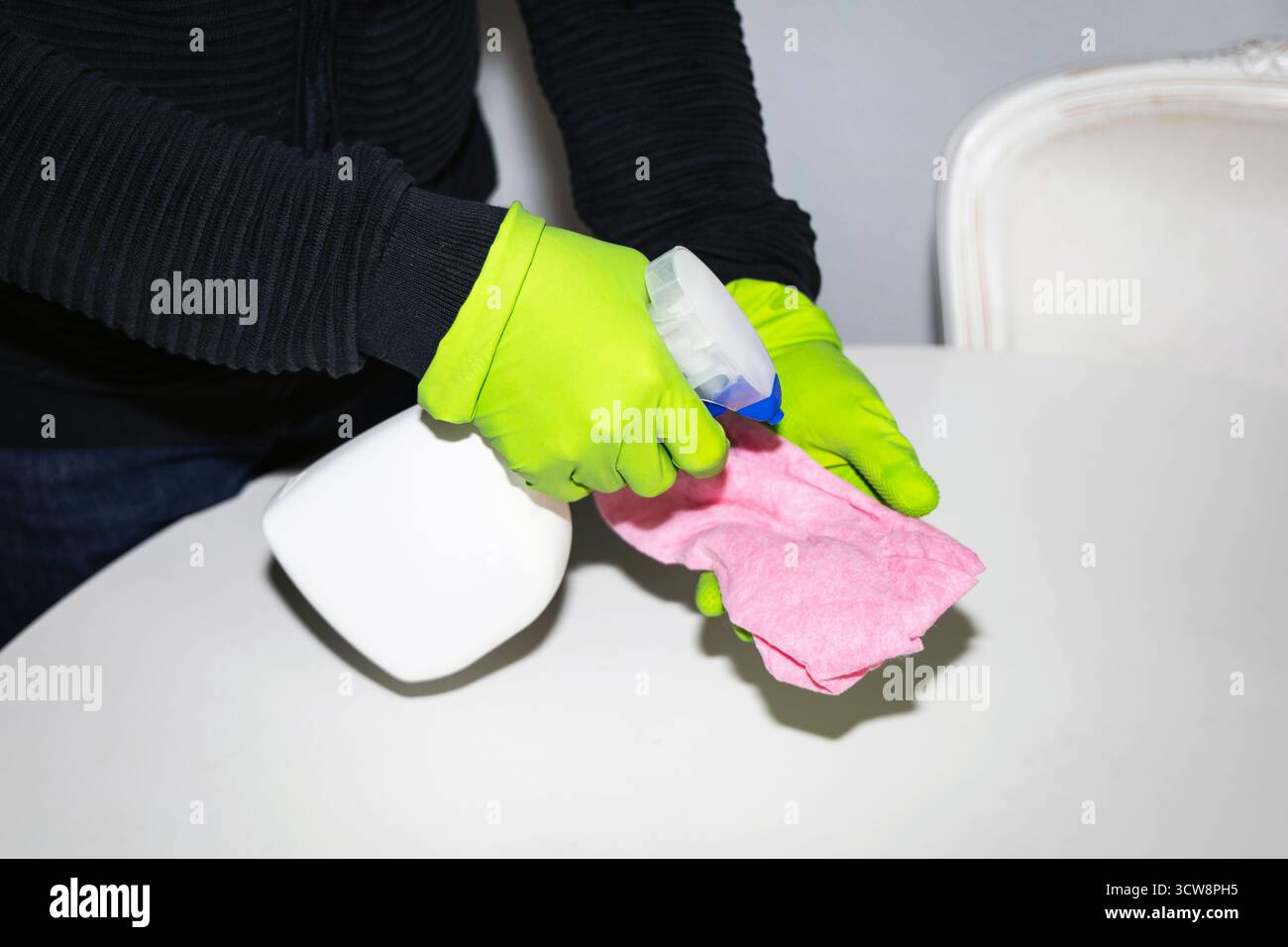 Une personne portant des gants en caoutchouc nettoyant la table à manger et utilisant un chiffon et un spray désinfectant, détergent. Concept de nettoyage et d'hygiène de la maison. Banque D'Images