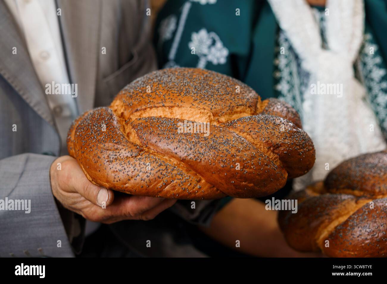 Gros plan d'une cérémonie de mariage juive avec un marié et une mariée tenant ensemble un pain challah rond recouvert de graines de pavot, symbolisant ble Banque D'Images