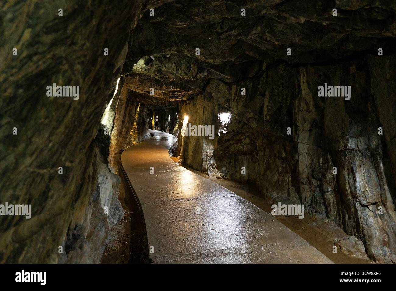 Ruskeala Mountain Park long chemin étroit, humide et pavé à l'intérieur d'un tunnel souterrain avec des murs de pierre rugueuse, éclairé par des projecteurs chauds le long de la sid Banque D'Images