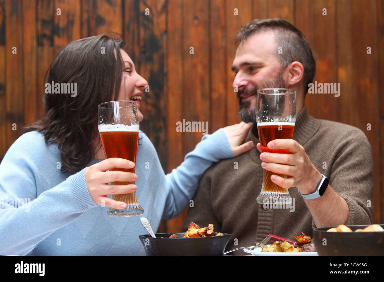 Joyeux couple d'âge moyen ludique dans un restaurant rustique dégustant des boissons et de la nourriture ensemble. Banque D'Images