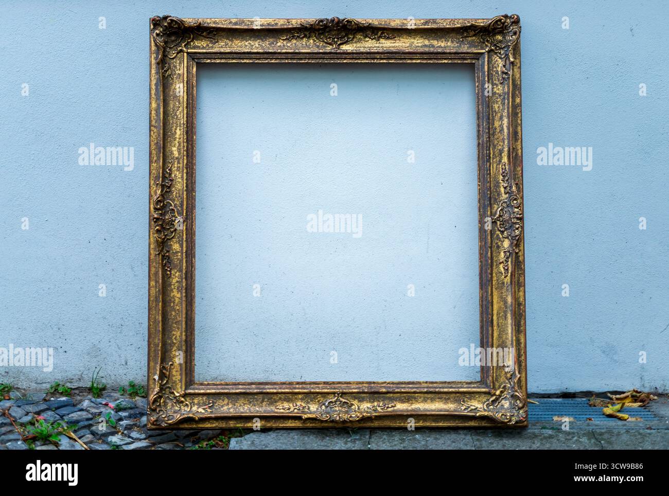 Vieux cadre d'image en or vintage appuyé contre un mur blanc, parfait pour les maquettes, la présentation d'œuvres d'art ou le fond de conception. Banque D'Images