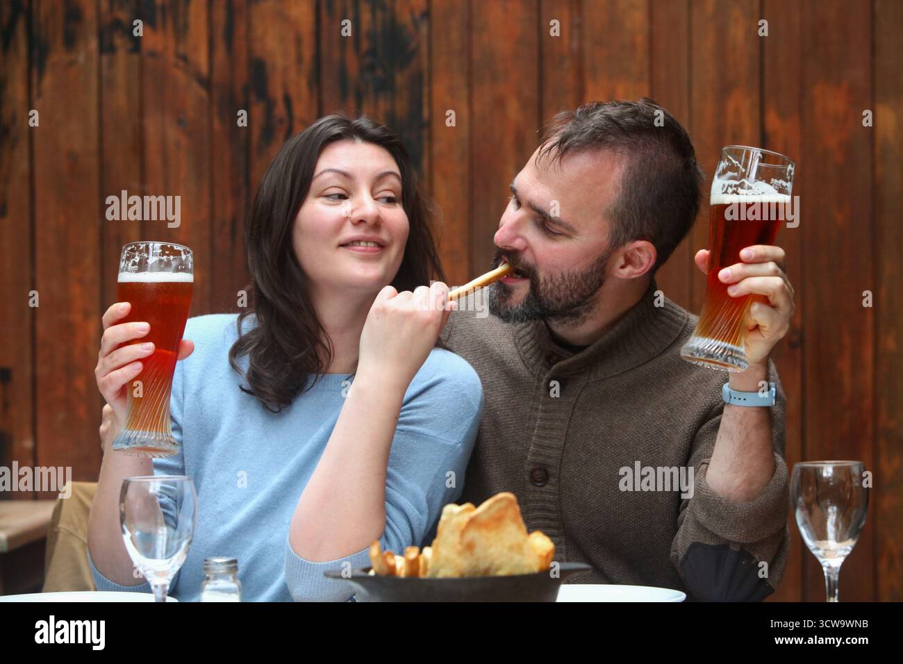 Joyeux couple d'âge moyen ludique dans un restaurant rustique dégustant des boissons et de la nourriture ensemble. Banque D'Images