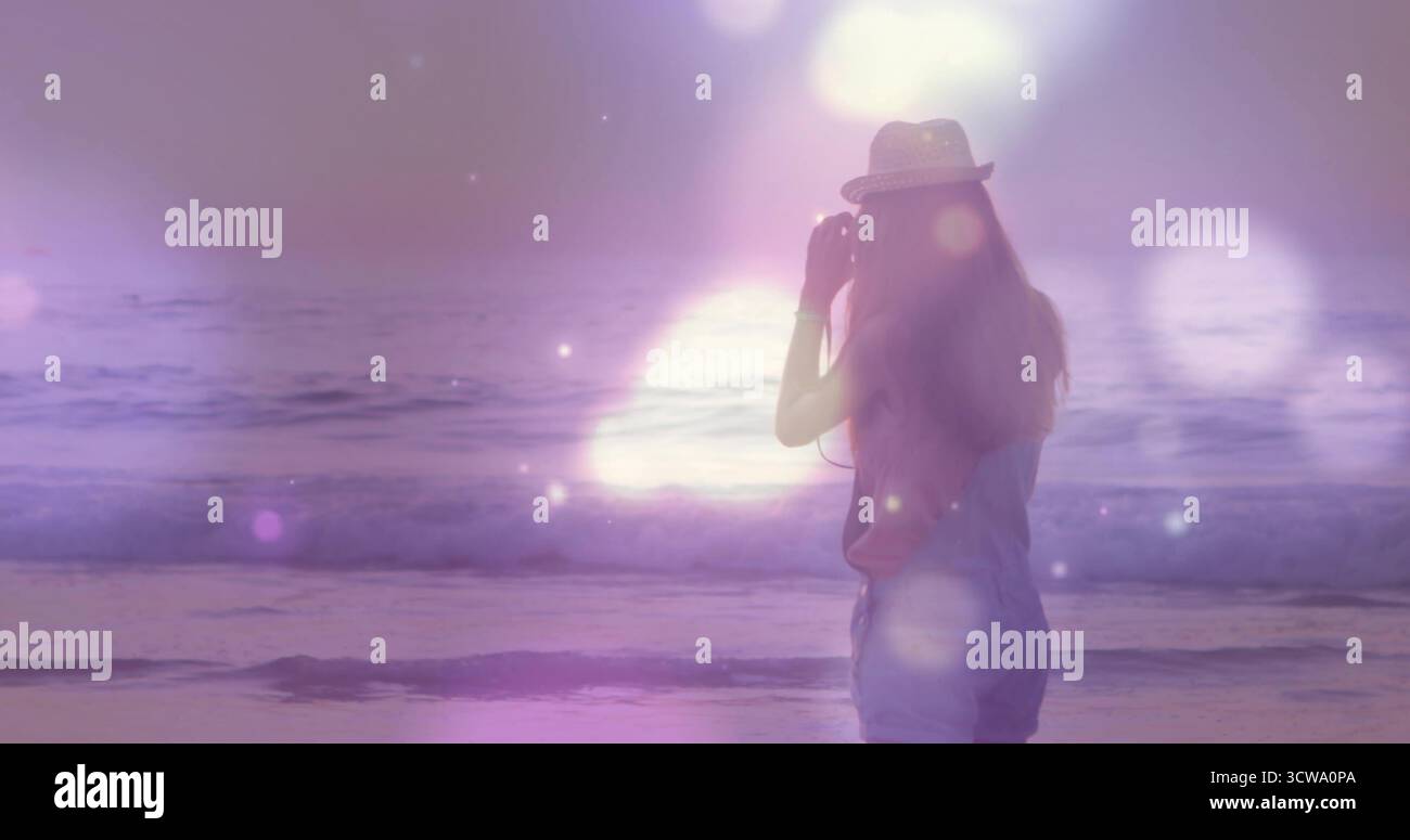 Contempler femme dans la Fedora de paille, combinaisons en denim face à l'horizon à la plage crépusculaire de lentille, espace de copie Banque D'Images
