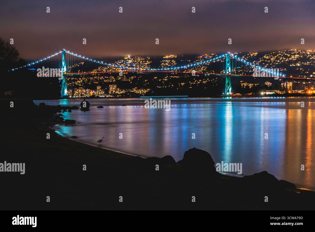 Vue nocturne d'un pont éclairé enjambant une rivière sombre, avec des lumières de la ville scintillantes dans l'eau. La scène capture la beauté tranquille et la vie urbaine. Banque D'Images