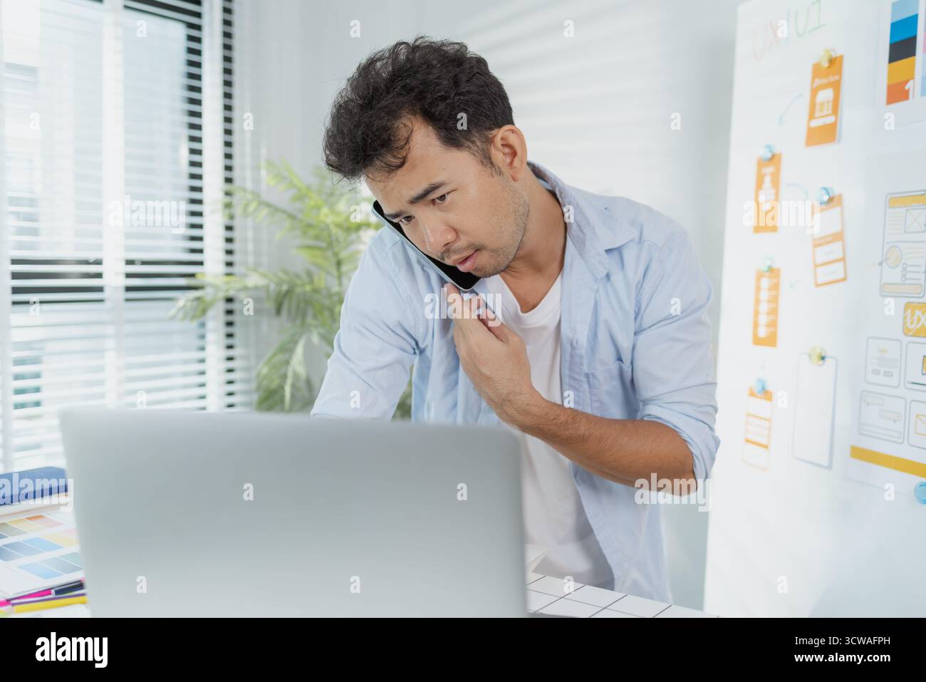 Un concepteur créatif travaille sur la planification UX/UI, analysant des croquis et des prototypes sur un tableau blanc tout en utilisant un ordinateur portable. Le processus montre la pensée de conception Banque D'Images