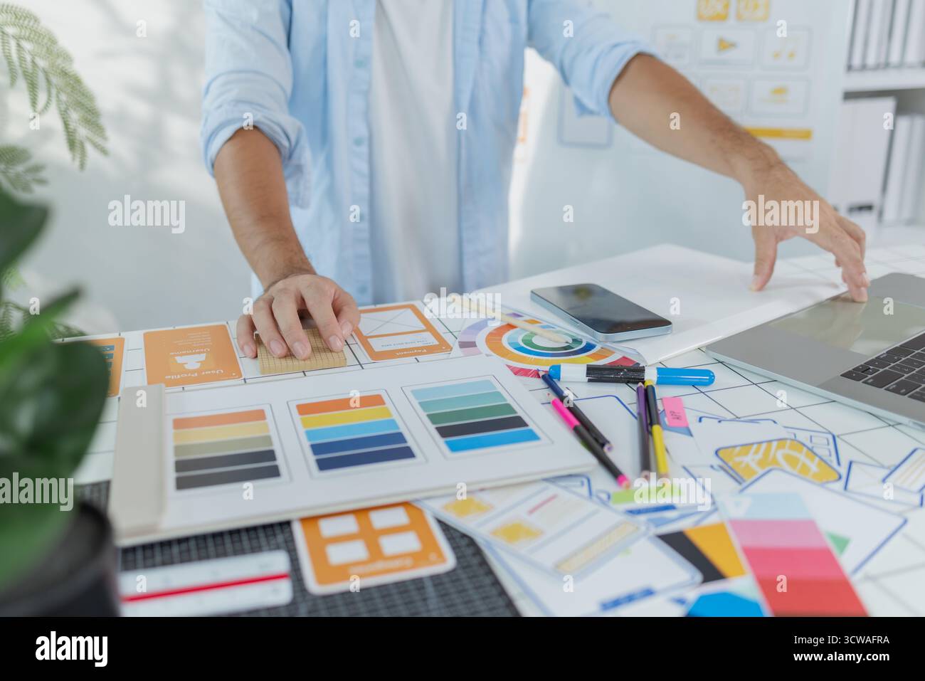 Un concepteur créatif travaille sur la planification UX/UI, analysant des croquis et des prototypes sur un tableau blanc tout en utilisant un ordinateur portable. Le processus montre la pensée de conception Banque D'Images