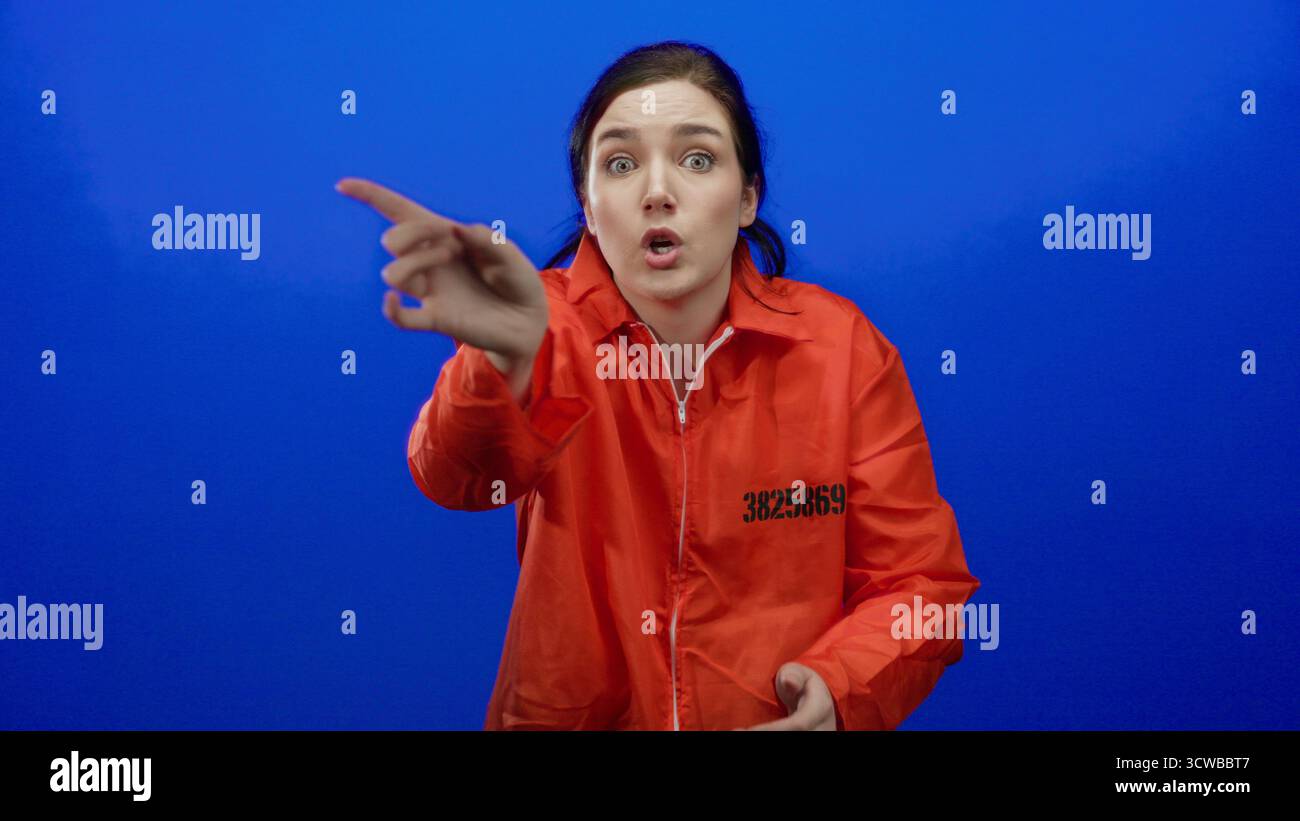Femme en combinaison de prison orange sur fond bleu exprime la frustration couvrant les oreilles et les gestes, soulignant l'intensité émotionnelle dans un confi Banque D'Images