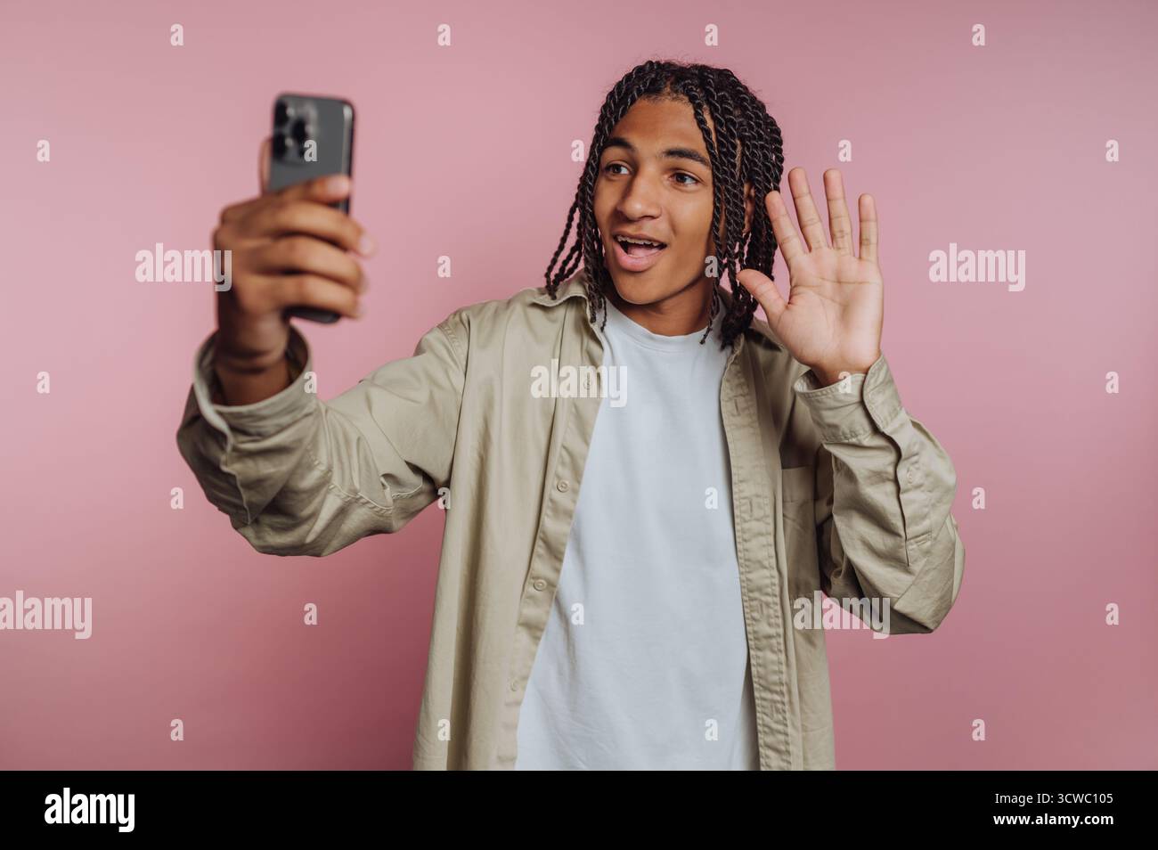 portrait de jeune homme ondule joyeusement à leur smartphone, incarnant une interaction amicale sur fond rose Banque D'Images