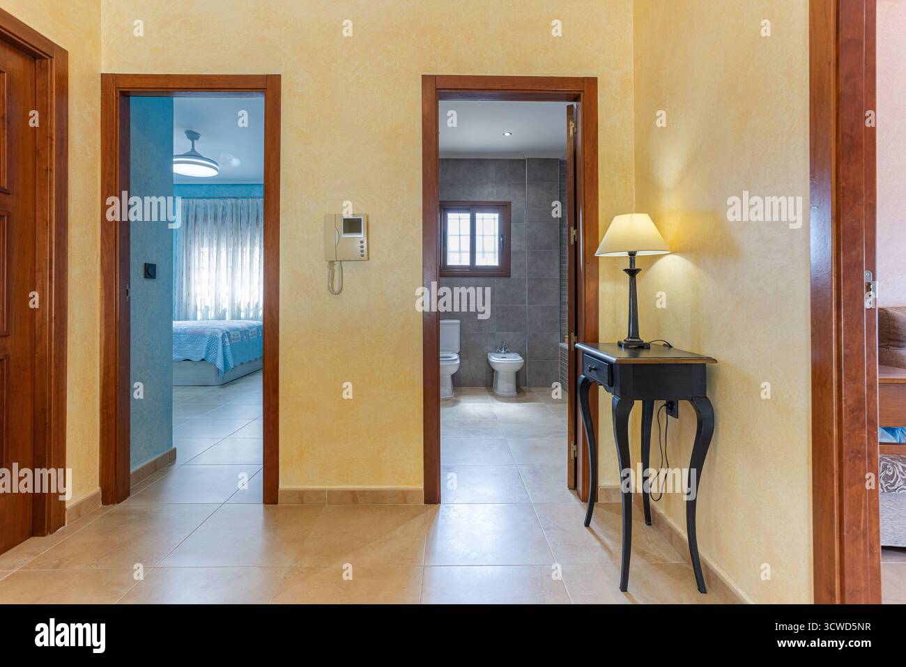 Couloir bien éclairé dans une maison contemporaine avec carrelage beige et murs texturés jaunes. Le couloir donne accès à une chambre avec Banque D'Images