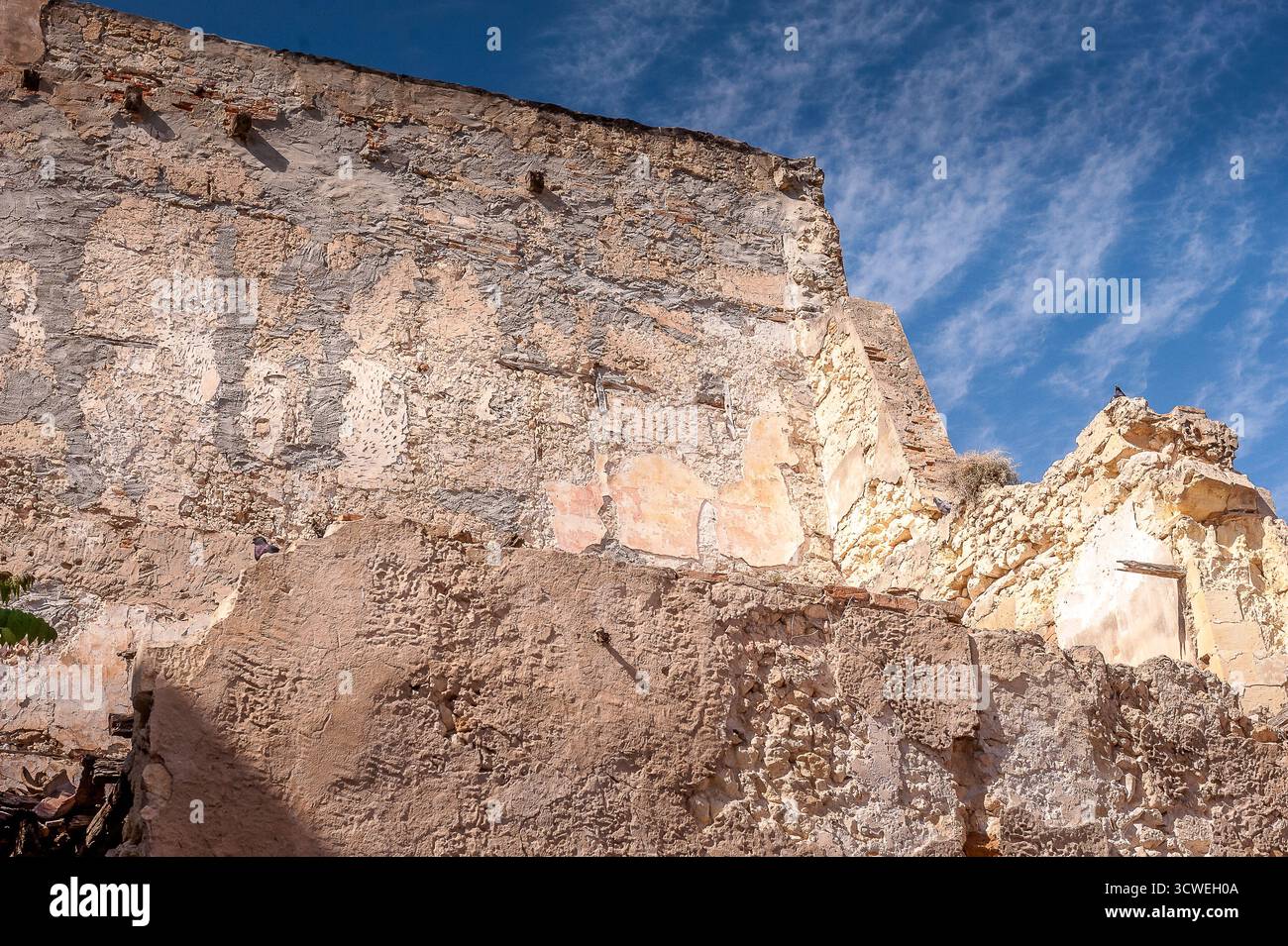 Ancien mur de pierre en ruine d'un bâtiment abandonné en Sardaigne, Italie, sous un ciel bleu vif avec des nuages éparpillés Banque D'Images