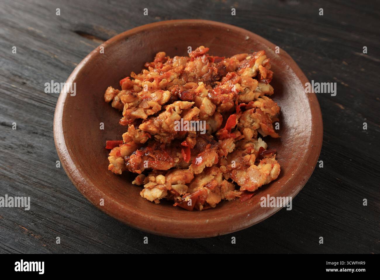 Gros plan Sambal Tempeh, tempe écrasé épicé sur une assiette en terre cuite Banque D'Images