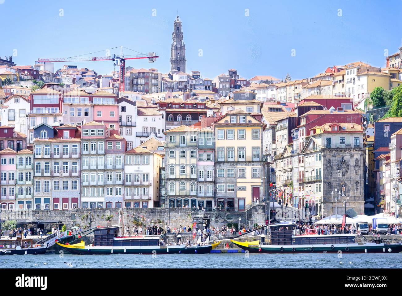 Vue détaillée du front de mer coloré et historique du quartier de Ribeira à Porto, animé par les gens et les bateaux, avec l'emblématique Tour Clérigos haut sur le t Banque D'Images