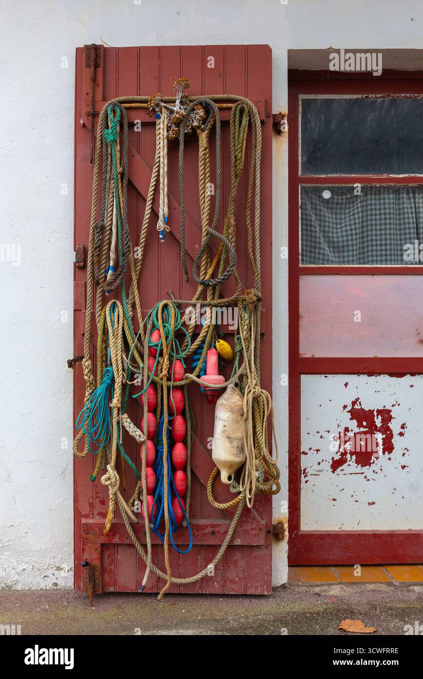 Le matériel de pêche, y compris les cordes et les bouées, pend à la porte d'une cabane de pêche. La porte est peinte en rouge avec un aspect rustique. Cordes diverses Banque D'Images