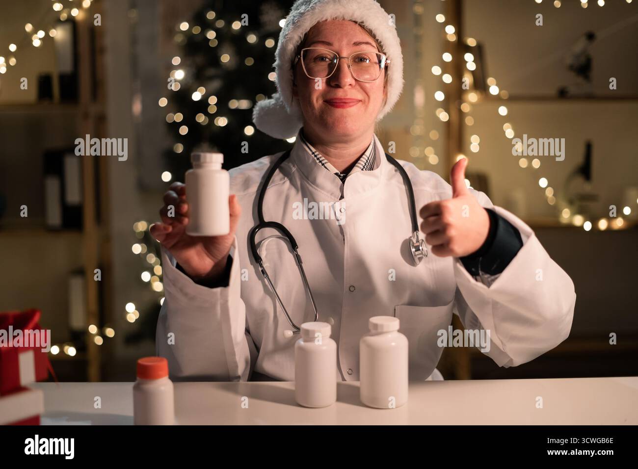 Concept de médecine, de santé et de vacances. Jeune femme médecin dans le chapeau de Père Noël recommandé bouteille de pilules pointant le pouce vers le haut dans OK bon geste tout en Wor Banque D'Images